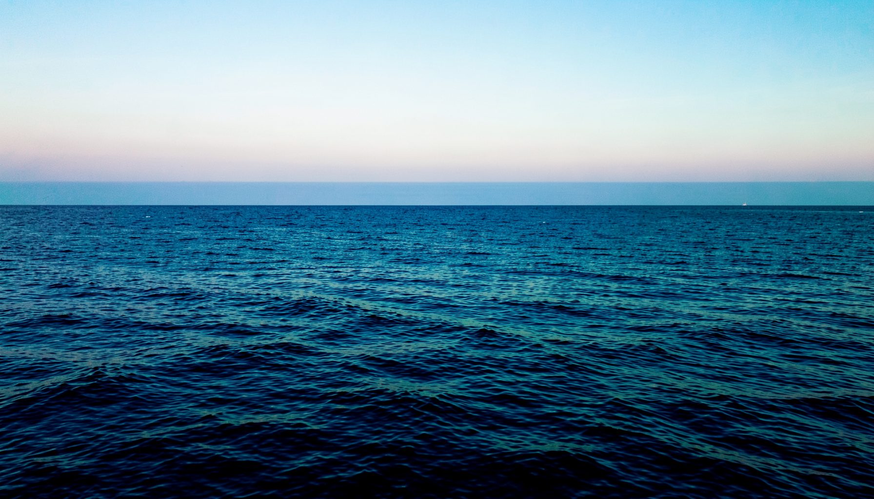 Wide panoramic view of a calm ocean horizon at dawn, blending deep navy blues with soft cyan and teal highlights, evoking clarity and forward momentum